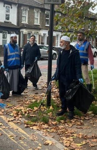 Volunteers in high-visibility vests collecting litter into bags on a residential street covered in autumn leaves